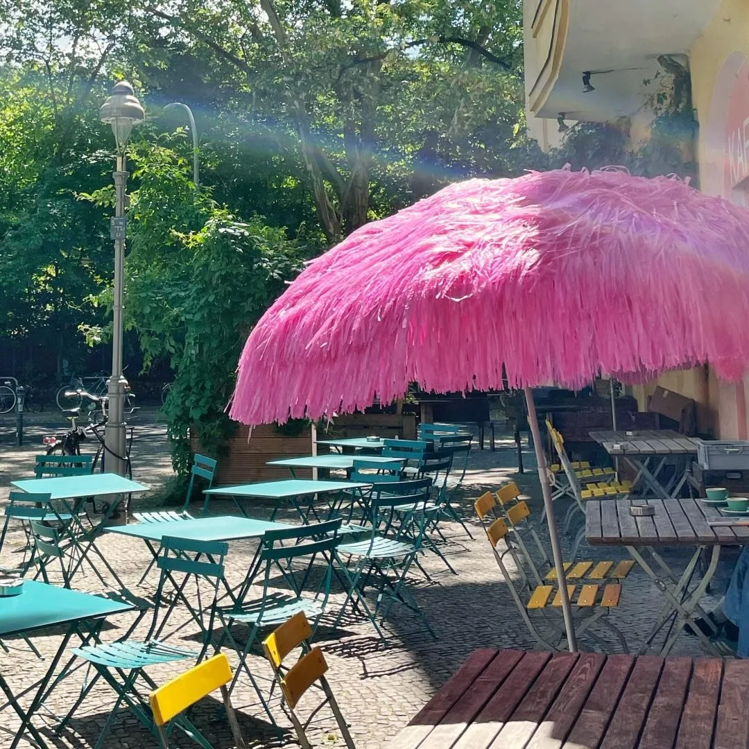Außenbereich mit pinkem Sonnenschirm und türkisen Stühlen